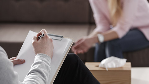 Close-up of therapist hand writing notes during a counseling session with a single woman sitting on a couch