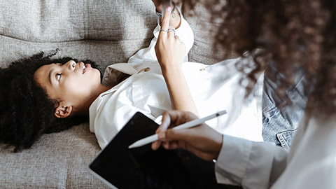 Client lying on sofa, therapist taking notes