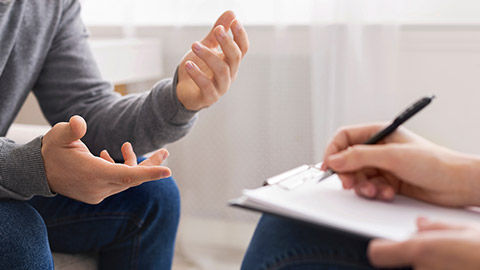 Psychotherapist writing notes, assessing patient's health and giving diagnosis to man sitting on couch during counseling session