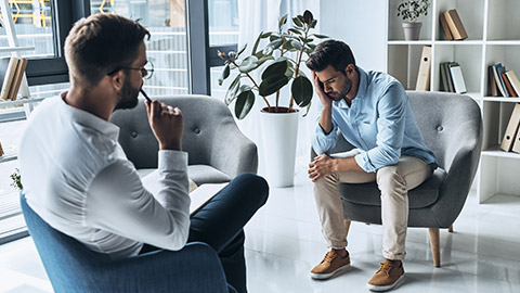 Feeling sadness. Young frustrated man solving his mental problems while having therapy session with psychologist