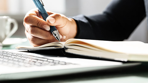 Hand holding pen and writing on notebook