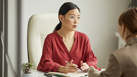 Portrait of successful Asian businesswoman talking to client while working at desk in white office cubicle, copy space