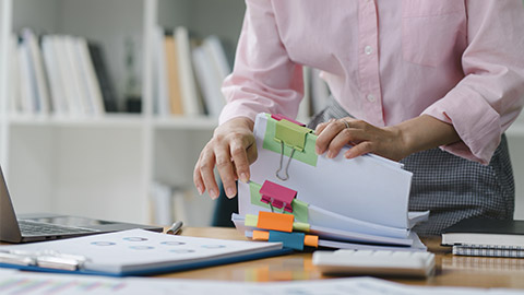 woman is sifting through stacks of paper files and folders that contain both incomplete and completed documents