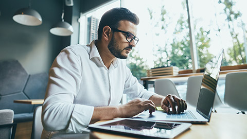 man wearing white shirt and eye glasses working with tablet and laptop