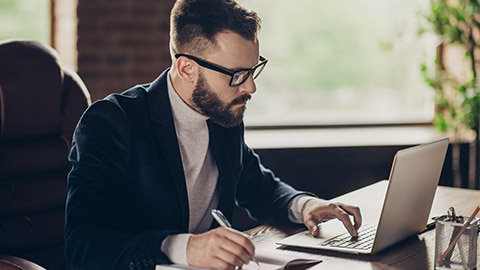 Elegant classic smart clever intelligent handsome attractive confident bearded ceo in black jacket and glasses, typing in laptop, writing start-up project strategy at modern work place, station