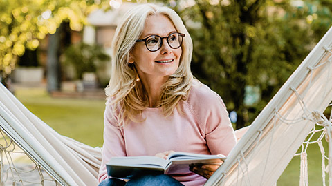 woman wearing glasses while reading in hammock in the summer garden