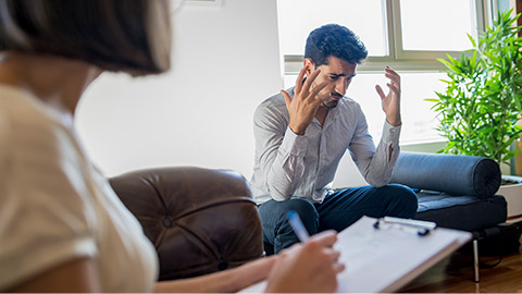 Psychologist taking notes during therapy session with an emotional man