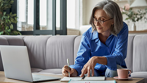 woman writing notes, and working using her laptop at home