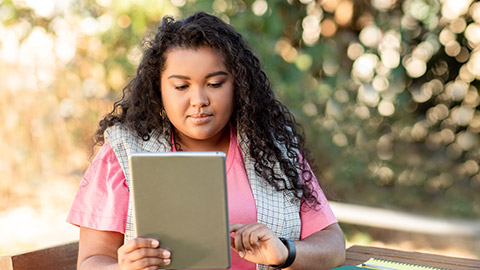 Hispanic lady student using digital tablet websurfing sitting at table in park