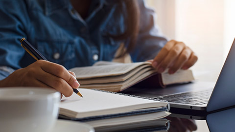 Casual young female student handwriting information on diary notebook while reading book and work on laptop computer