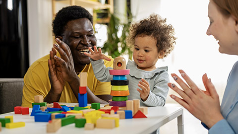 Mother and father supporting their cute little daughter in playing with colorful didactic wooden toys at home