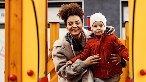 Achildcare worker supervising a child on outdoor play equipment