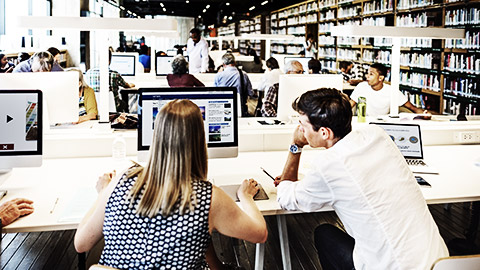 People in library using a computer and some getting books