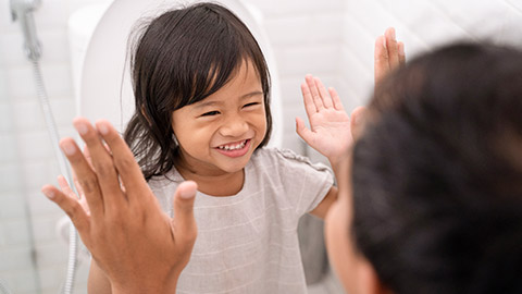 A small child smiling and giving a high five to an adult