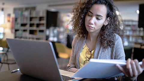 woman doing research on library with laptop and notes