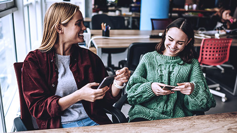 Two woman communicating while laughing holding their phones