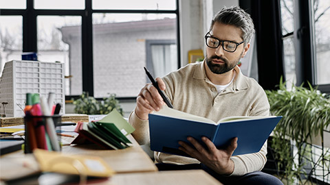 A handsome businessman with a beard sits at a desk in a modern office