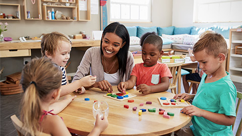 Teacher And Pupils Using Wooden Shapes In Montessori School