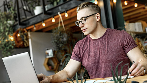 Young man looking at his laptop while notetaking