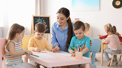 Little children with kindergarten teacher drawing at table indoors.