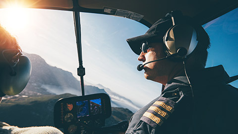 Over-the-shoulder view of a pilot flying a Robinson R44 helicopter