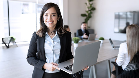 Smiling entrepreneur woman while holding a laptop looking at the camera