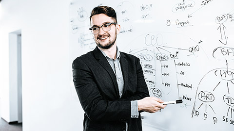 Young attractive dark-haired man is writing a business plan and smiling on whiteboard