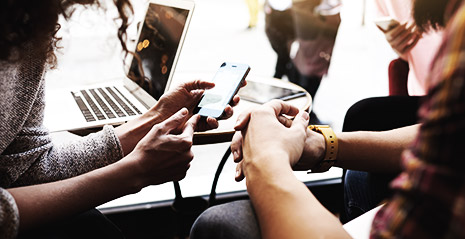 A group of people in a cafe using a phone, a laptop all while talking to each other