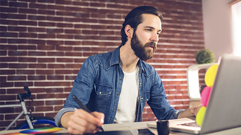 Creative businessman writing on graphic tablet while using laptop in office