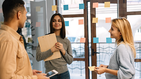 Group of young happy entrepreneurs planning start up project, discussing strategy, talking, working together using scrum and sticky notes in office