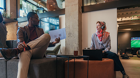 Multiracial colleagues discussing paperwork at office while sitting on grey orange sofa