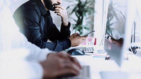 Man on dark suite using phone with co-worker on his side