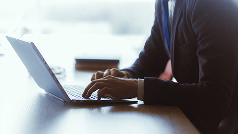 A close image of a person's hand using a laptop thats tilted slightly away from others