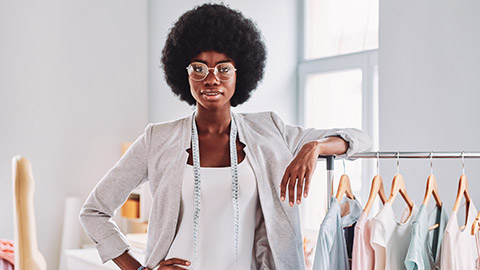 The owner of a clothing store standing amongst some of their inventory