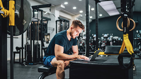 A fitness trainer sitting at a table, referring to their notes while writing up an incident report on a laptop