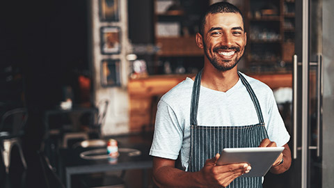 A smiling employee standing in a restaurant holding a tablet device