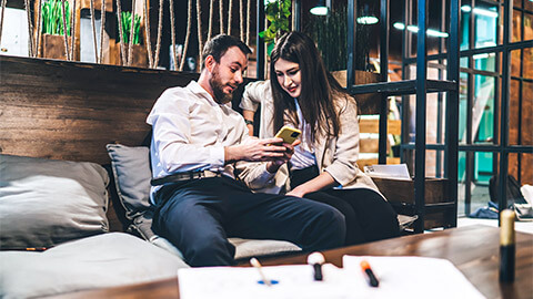 A manager seated with a colleague, sharing sensitive information on their smart phone with a colleague