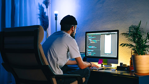 Young man mobile developer writes program code on a computer, programmer work in home office.