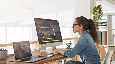 Side view portrait of female IT developer typing on keyboard with black and orange programming code on computer screen