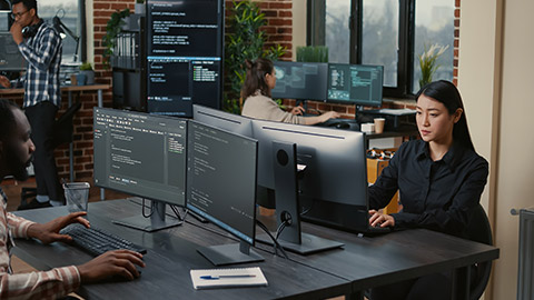 Two focused coders facing each other writing code in software development office while team of coders are developing artificial intelligence