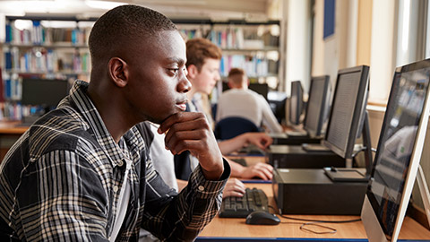 Male Student Working On Computer In College Library