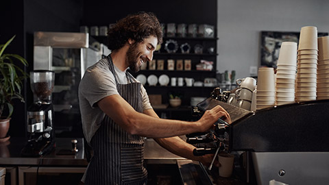 Smiling man with apron preparing coffee for customer in his small business