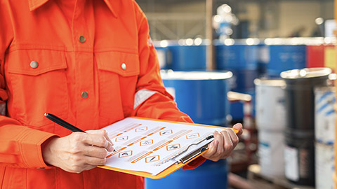 Action of safety officer is using a pen to checking on the hazadous material symbol label form with the chemical barrel as blurred background