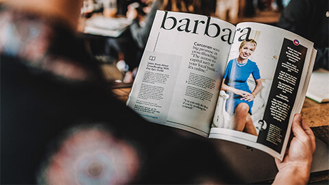 A professional in a common area at their workplace, scanning through a magazine