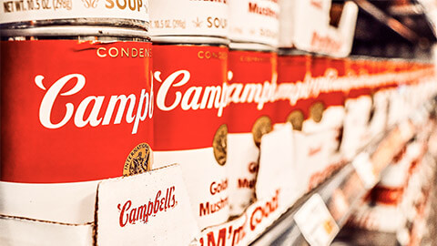 A row of Campbell's Soup cans on a supermarket shelf