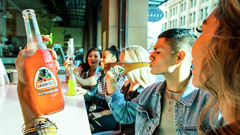 A person holding up a glass bottle of soda, while seated in a restaurant