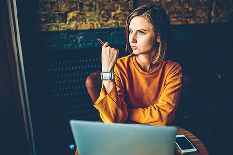 A UX Designer seated in front of their laptop, looking onwards while thinking through a particular problem