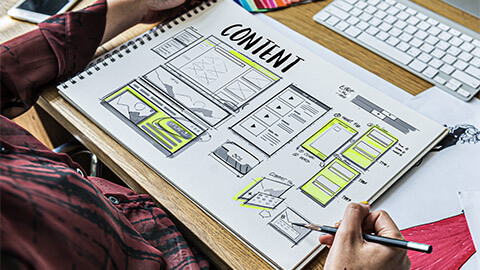 A designer wireframing a webpage at their desk, in a notebook