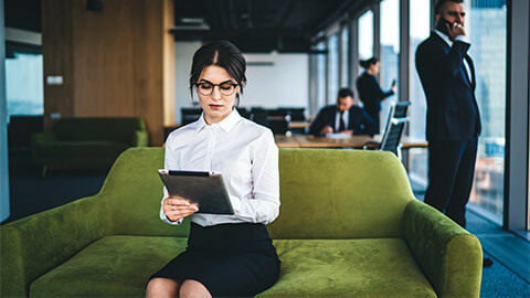 A project manager seated in a common area in their office, using a project management tool on a tablet