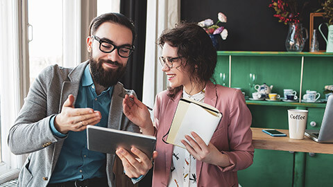 2 designers discussing the progress of a project while viewing it on a tablet device